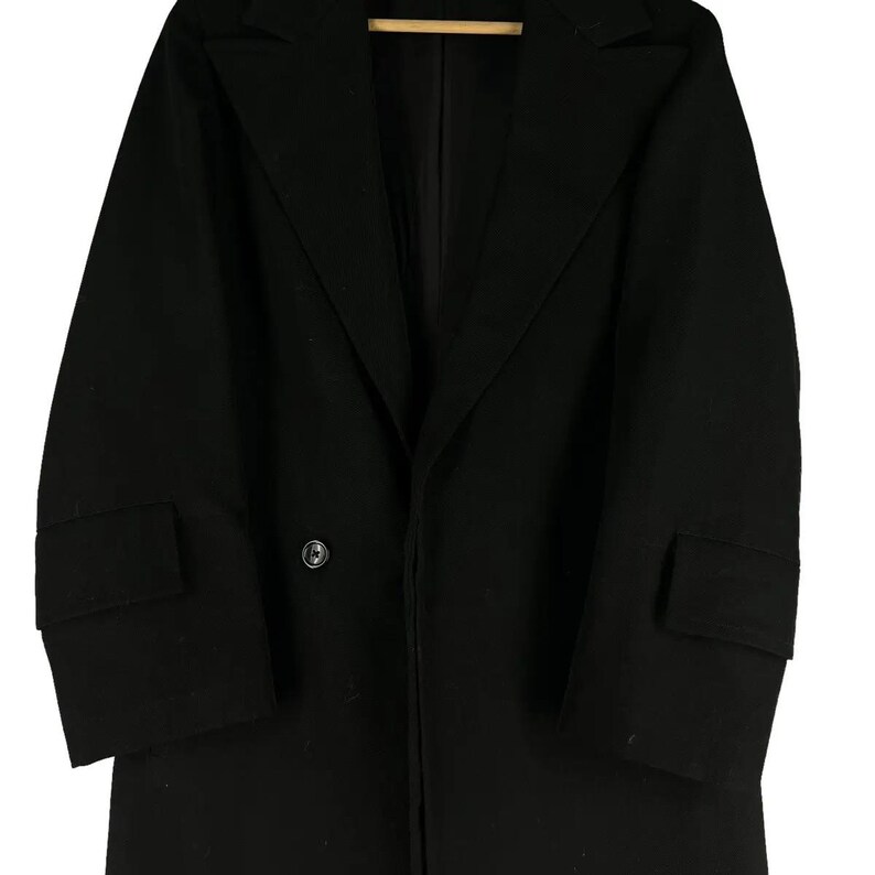 May include: A black double-breasted coat with a notched lapel and two front pockets. The coat has a single button closure and a classic, tailored design. The coat is made of a solid black fabric.