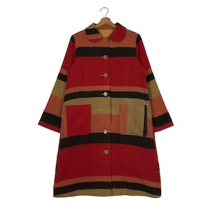 May include: A vintage, long coat with a colorful striped pattern. The coat features a red base with black, brown, and tan stripes. It has a rounded collar, button closures, and two front pockets. The coat is hanging on a wooden hanger.