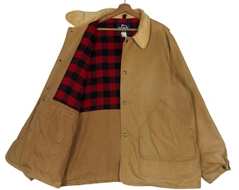 May include: A tan canvas jacket with a plaid flannel lining. The jacket has a button closure, two pockets on the front, and a single pocket on the inside.