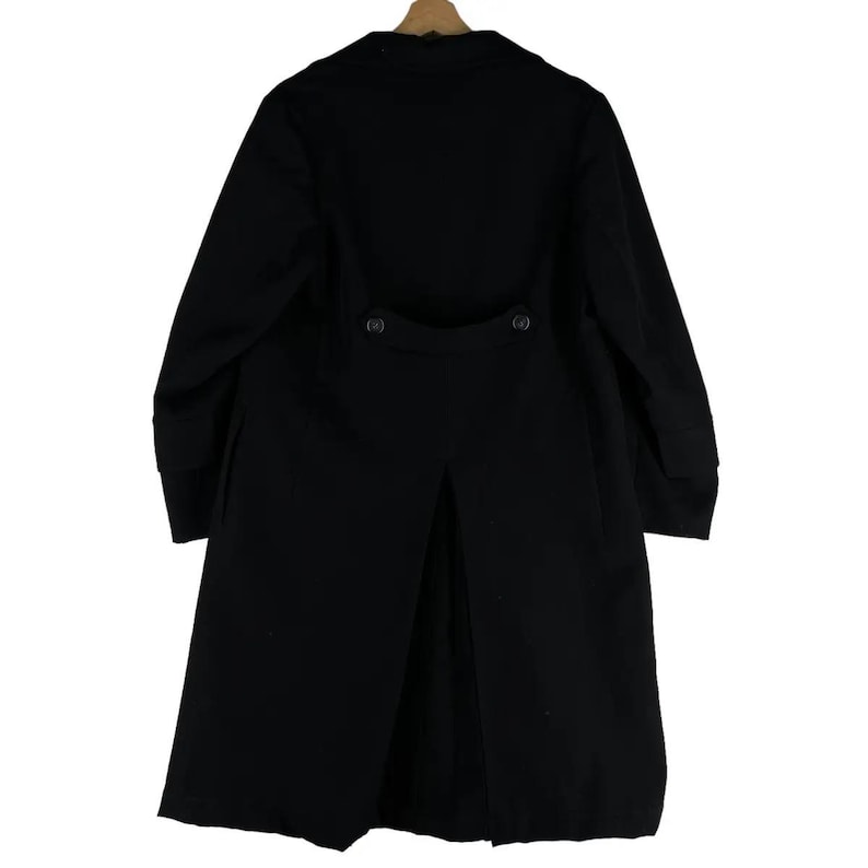 May include: A long, black coat with a classic design. The coat features a button closure, a notched collar, and a split back. The coat is hanging on a wooden hanger.