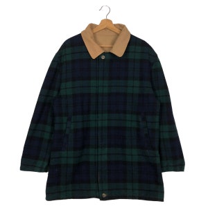 Può includere: Giacca a quadri blu navy e verde, con colletto beige e chiusura con bottoni. La giacca è appesa a un'appendiabiti in legno. Il motivo a quadri è classico.