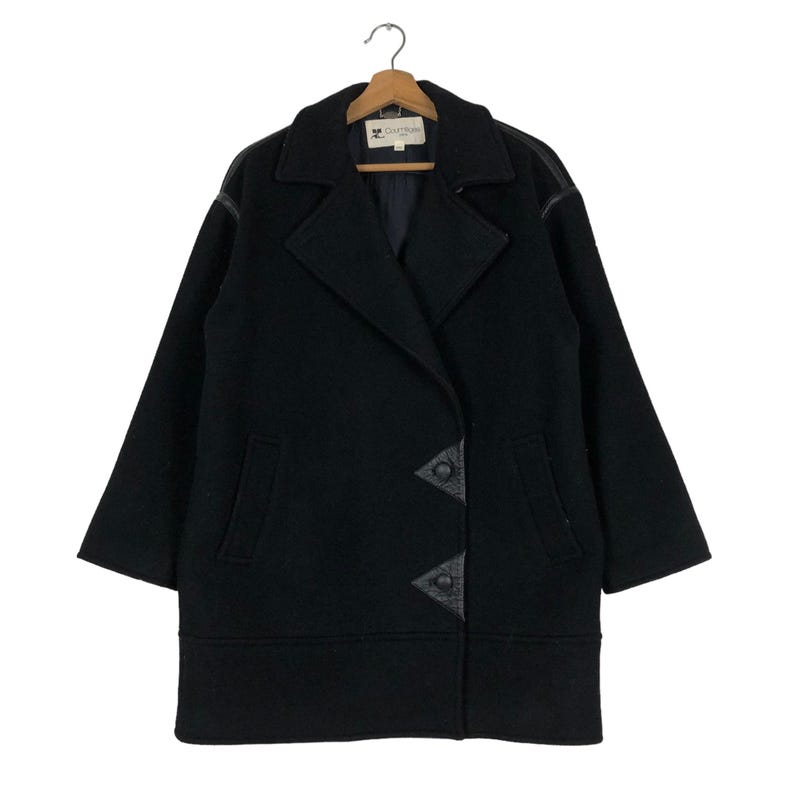 May include: A black wool coat with a double-breasted design, featuring leather accents on the lapels and front closure. The coat has a classic collar, two front pockets, and is hanging on a wooden hanger.
