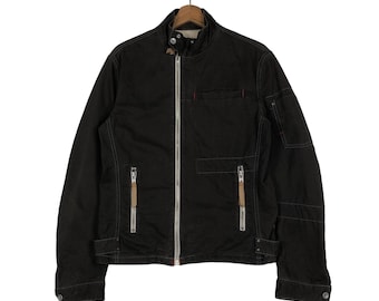 May include: A black jacket with a full-length silver zipper, two front pockets with zippers, and a small pocket on the chest. The jacket has a stand-up collar and is hanging on a wooden hanger.