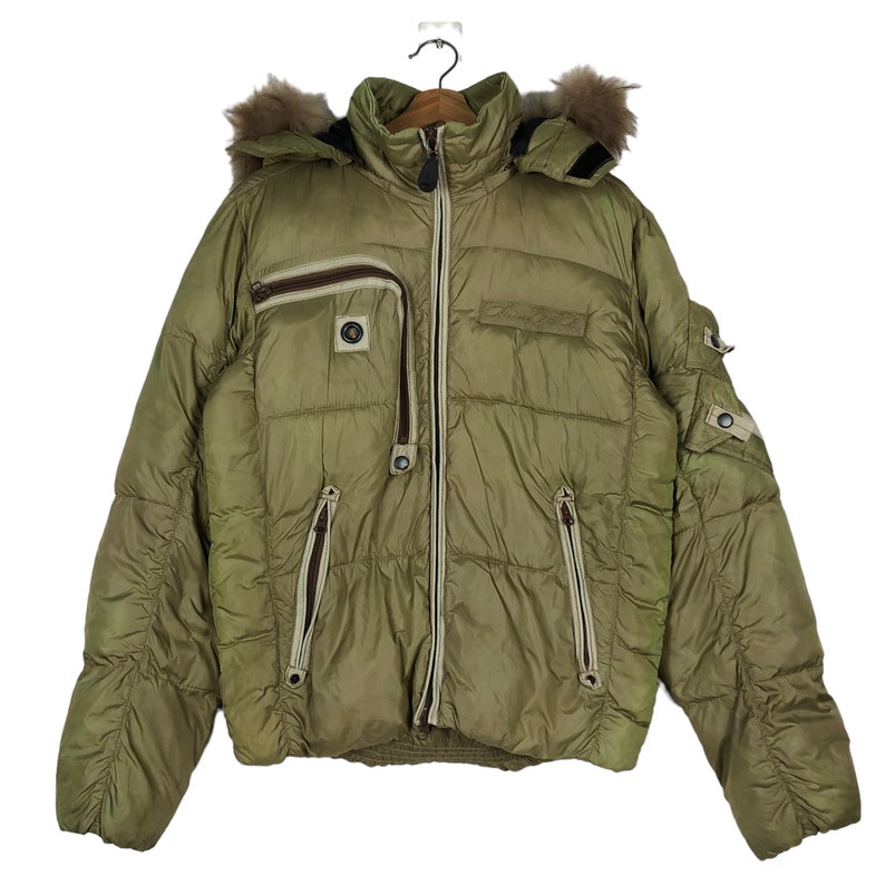 Puede incluir: Una chaqueta acolchada verde con capucha forrada de piel y varios bolsillos con cremallera.