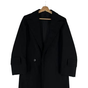May include: A black overcoat with a notched collar and two front pockets. The coat has a double-breasted closure with two buttons and is hanging on a wooden hanger.
