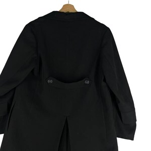May include: A black coat with a classic design, featuring a notched lapel and two decorative buttons on the back. The coat is hanging on a wooden hanger, showcasing its tailored silhouette and formal style.