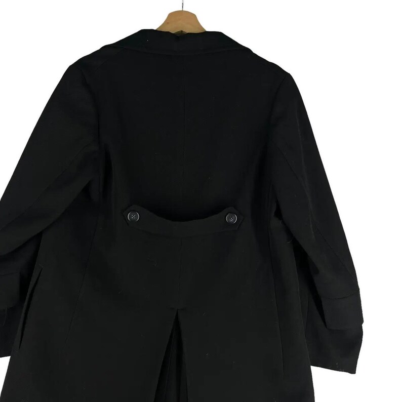 May include: A black coat with a classic design, featuring a notched lapel and two decorative buttons on the back. The coat is hanging on a wooden hanger, showcasing its tailored silhouette and formal style.