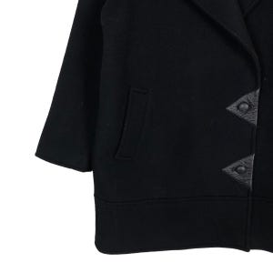 May include: Black wool coat with a notched collar, a single pocket, and three-quarter sleeves. The coat features leather triangle-shaped button closures. The hemline is straight and the coat appears to be a mid-length style.