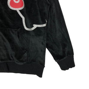 May include: Black velour hoodie with a silver and red graphic on the front. The graphic is a stylized cartoon character.