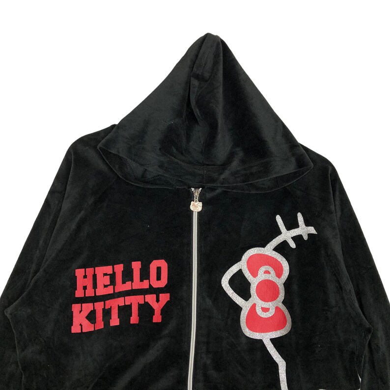 May include: Black velour zip-up hoodie with a red "Hello Kitty" graphic and a silver glitter Hello Kitty illustration.