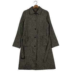 May include: A long, grey tweed coat with a collared neckline and a matching belt. The coat has a button-down front, two front pockets, and long sleeves. The coat is hanging on a wooden hanger.