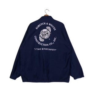 May include: Navy blue work jacket with the Babcock & Wilcox Construction Co. logo on the back. The logo is a white circular design with the text "B&W" and the phrase "I TAKE II FOR SAFETY".