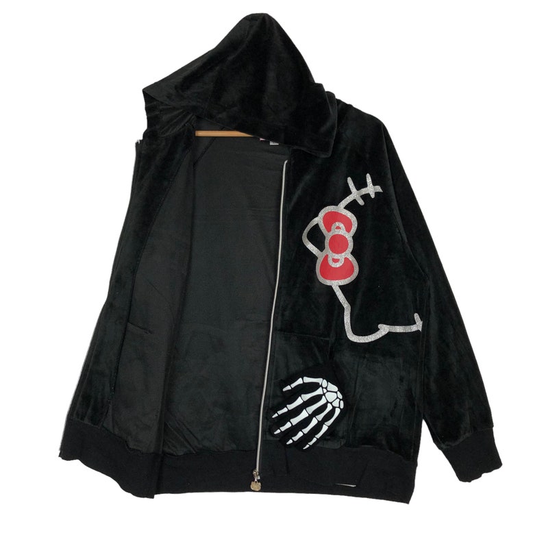 May include: Black velour hooded zip-up jacket with a Hello Kitty graphic on the right side and a skeleton hand graphic on the left side.