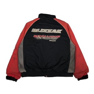 May include: Black, red, and gray racing jacket with the text "BLIZZAK REVOLUTION" and "Bridgestone" printed on the back. The jacket has a stand-up collar, a black ribbed hem, and red sleeves.