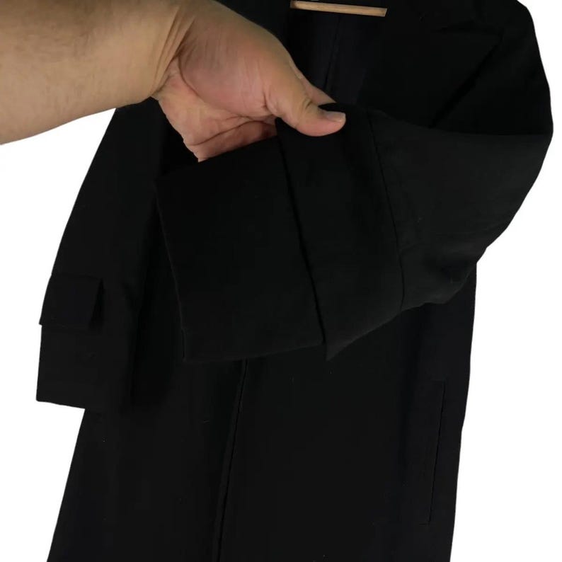 May include: A black blazer with long sleeves. The blazer has a classic design with a notched lapel and a single-button closure. The sleeves have a cuff detail. The fabric appears to be a smooth, woven material.