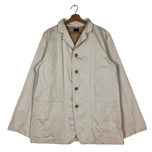 May include: A cream-coloured utility jacket with a button-up front, two chest pockets, and a collar. The jacket has a slightly distressed look.