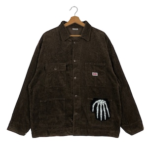 May include: Brown corduroy jacket with a button-up front, two chest pockets, and two lower pockets. A small rectangular patch is on the chest, and a black patch with a white skeleton hand is on the lower pocket.
