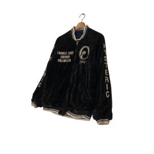 May include: Black velvet bomber jacket with white embroidered lettering that reads "TRANCE LOVE ENERGY UNLIMITED 1984" and "HYSTERIC" on the sleeves.
