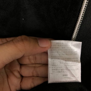 May include: White care tag with black text detailing washing instructions for a garment. The text reads: "Tumble dry low. Use non-fluorescent detergent. Do not use fabric softener. Wash separately as color may bleed. Do not soak. Do not wring. Do not iron. Avoid rubbing the decorative parts.  Made in China."