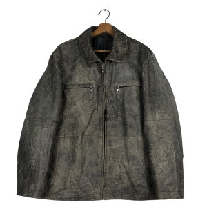 May include: A distressed-look, gray leather jacket with a zip-up front and two chest pockets. The jacket hangs on a wooden hanger against a white background. The leather has a textured appearance.
