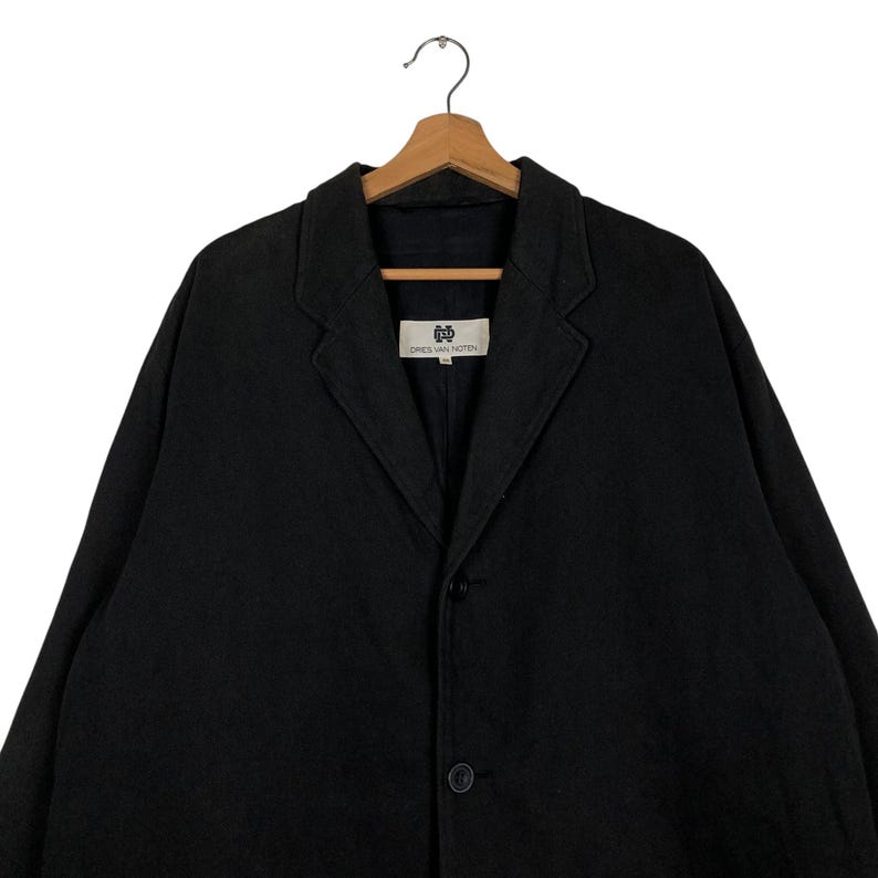 Może przedstawiać: Czarny wełniany blazer z jednorzędowym zapięciem i etykietą z napisem "DRIES VAN NOTEN".