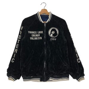 May include: Black velvet bomber jacket with white lettering that reads "HYSTERIC" on the sleeves and "TRANCE LOVE ENERGY UNLIMITED 1984" on the front. The jacket has a white collar and white ribbed cuffs and hem.