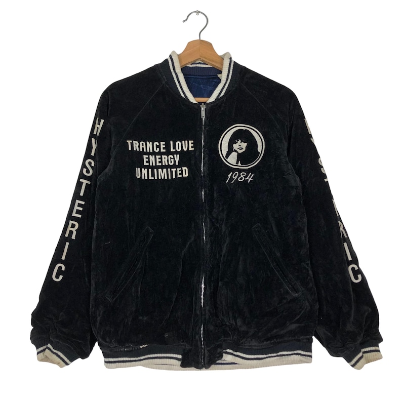May include: Black velvet bomber jacket with white lettering that reads "HYSTERIC" on the sleeves and "TRANCE LOVE ENERGY UNLIMITED 1984" on the front. The jacket has a white collar and white ribbed cuffs and hem.