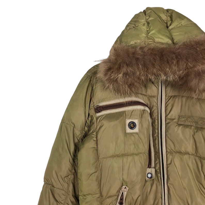 Puede incluir: Una chaqueta acolchada verde con capucha forrada de piel marr&oacute;n. La chaqueta tiene cierre de cremallera y varios bolsillos.