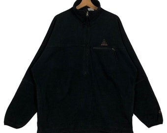 May include: Black fleece pullover with a half-zip closure and a small pocket on the chest. Features a high collar and a drawstring at the hem. The Nike ACG logo is visible on the chest.