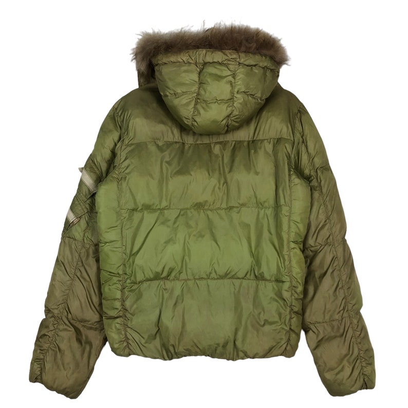 Puede incluir: Una chaqueta acolchada verde con capucha forrada de piel. La chaqueta tiene un dise&ntilde;o acolchado y una cremallera.