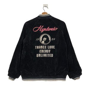 May include: Black velvet bomber jacket with a white and black striped collar and cuffs. The back of the jacket features a pink and white graphic with the text "Hysteric 19 84 Trance Love Energy Unlimited".