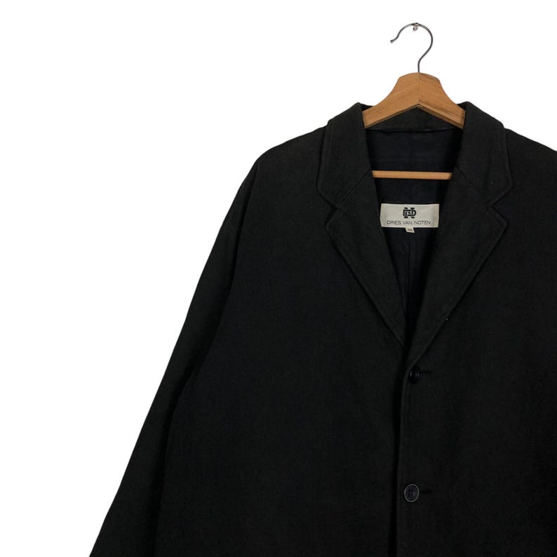 Może przedstawiać: Czarny, długos rękawowy blazer z jednorzędowym zapięciem i dwoma guzikami ozdobnymi. Blazer ma metkę z napisem "DRIES VAN NOTEN".