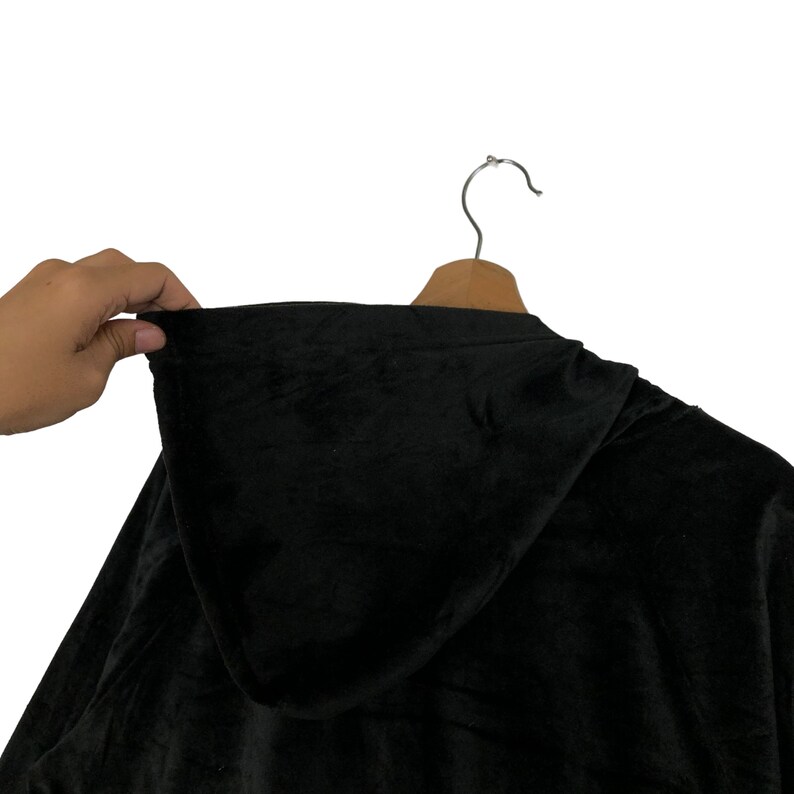 May include: Black hooded sweatshirt made of soft velour fabric. The hood is lined with the same fabric and has a drawstring.