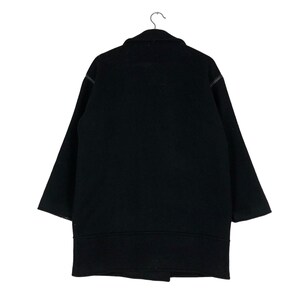 May include: A black wool coat with a classic design, hanging on a metal hanger. The coat features a wide collar, long sleeves, and a mid-thigh length. The coat is a solid black color.