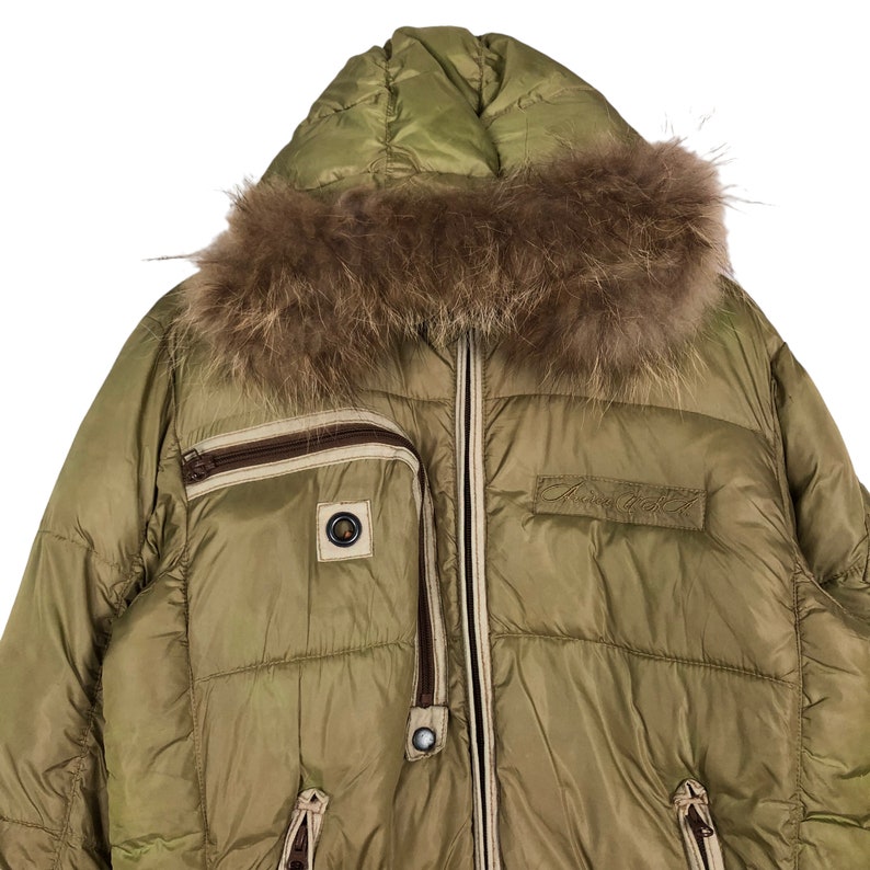 Puede incluir: Una chaqueta acolchada verde con capucha forrada de piel marr&oacute;n. La chaqueta tiene cierre de cremallera y varios bolsillos. El nombre de la marca "Andrea Dett" est&aacute; bordado en la parte delantera.