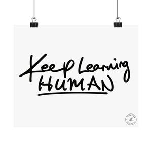 May include: A white rectangular poster featuring the black handwritten text Keep Learning HUMAN. The poster is held by two black metal clips at the top. A small circular logo with the text ANALOG VIRTUE is visible in the bottom right corner.