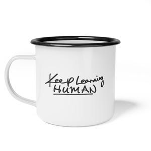 May include: A white enamel mug with a black rim and a matching white handle. The front of the mug features the black handwritten-style text Keep Learning HUMAN with a horizontal line underneath the word HUMAN, centered on the smooth surface.