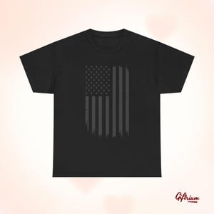 Puede incluir: Camiseta negra con un gráfico de bandera estadounidense gris desgastado.