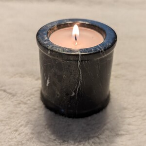 May include: A black marble candle holder with a white candle burning inside.