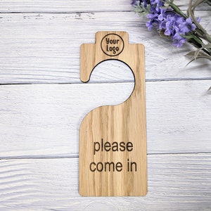 May include: Wooden door hanger with a hook at the top and the text "please come in" engraved on the front. The hanger also has a circle at the top with the text "Your Logo" inside.