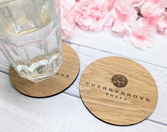 Könnte beinhalten: Zwei runde Untersetzer aus hellem Holz mit einem Glas Wasser. Ein Untersetzer trägt das Wort "LOVE". Der andere zeigt den Text "CHERRYGROVE CRAFT" und ein Baumlogo.