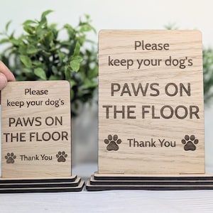 May include: Two wooden signs with the text "Please keep your dog's paws on the floor. Thank you." The signs are on a black stand.