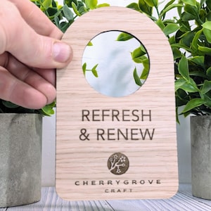 May include: Wooden door hanger with a round cutout and the text "REFRESH & RENEW" in a brown font. The bottom of the hanger has the text "CHERRY GROVE CRAFT" in a smaller font.