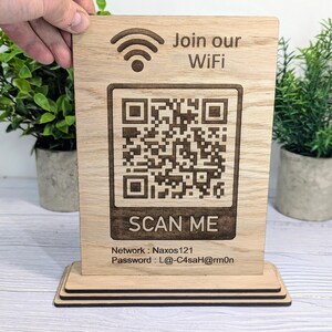 May include: Wooden sign with a QR code and the text "Join our WiFi" and "SCAN ME". The sign also includes the network name "Naxos121" and the password "L@-C4saH@rm0n".