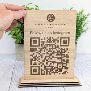 May include: A wooden sign with a laser-engraved QR code and the text "CHERRYGROVE CRAFT Follow us on Instagram". The sign is on a wooden stand.