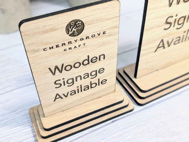 May include: Wooden sign with the text "Cherry Grove Craft" and "Wooden Signage Available". The sign is made of light brown wood and has a black border.