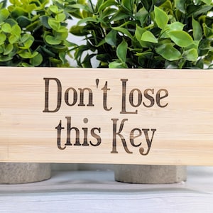 May include: A wooden key holder with the text "Don't lose this key" engraved on it. The key holder has a metal ring for attaching keys.
