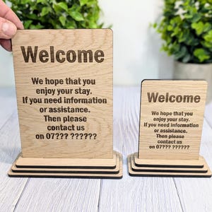 May include: Two wooden signs with the text "Welcome" and a message welcoming guests and providing a phone number for contact. The signs are on wooden stands.
