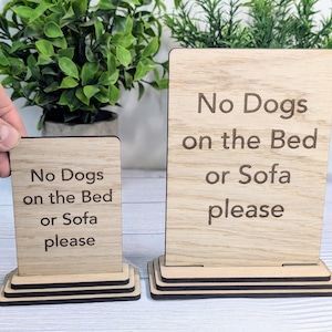 May include: Two wooden signs with the text "No Dogs on the Bed or Sofa please" on them. The signs are on a wooden stand.