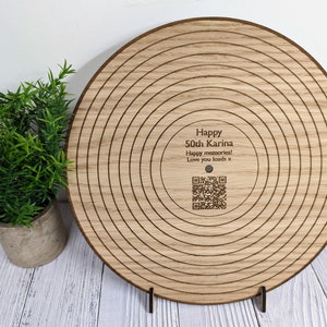 May include: A wooden record-shaped plaque with concentric circles engraved on the surface. The plaque has a message that reads "Happy 50th Karina Happy memories! Love you loads x" and a QR code.